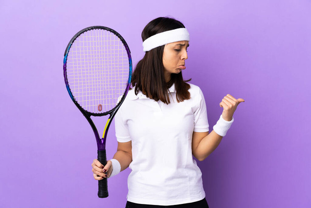 Young woman tennis player over isolated background unhappy and pointing to the side - Photo, Image