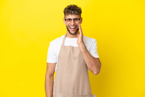 Serveur restaurant homme blond isolé sur fond jaune avec surprise et expression faciale choquée - Photo, image