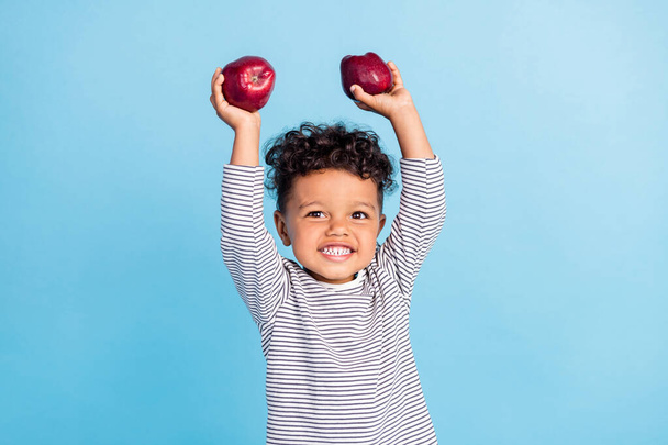 Portrait of attractive cheerful boy baby holding in hands rising up apples isolated over bright blue color background - Photo, image