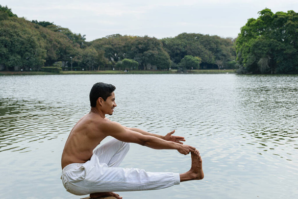 Sao Paulo, SP, Brasil, julio 16 2021. Mujer de 40 años con espalda rasgada sentada sobre sus pies en una posición de yoga en un parque público. - Foto, Imagen