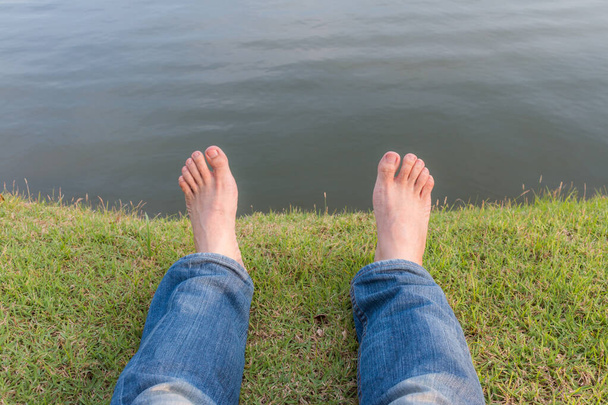 Descanse y relájese pies desnudos sobre hierba verde con fondo natural del lago - Foto, Imagen