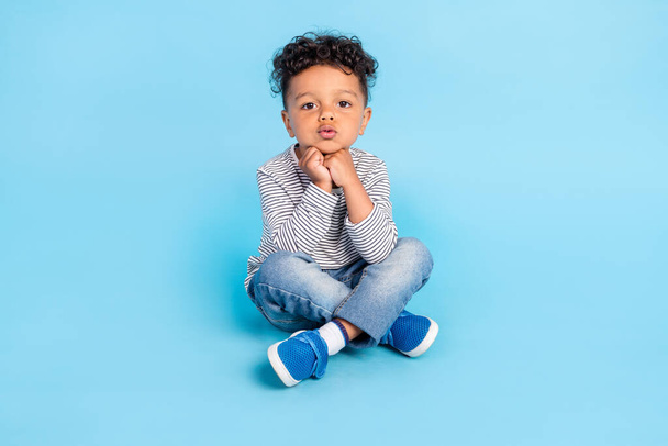Portrait of attractive focused boy sitting on floor lotus pose watching isolated over bright blue color background - Valokuva, kuva
