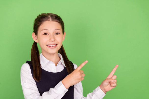 Photo of young school girl happy positive smile indicate fingers empty space ad advise promo isolated over green color background - Zdjęcie, obraz