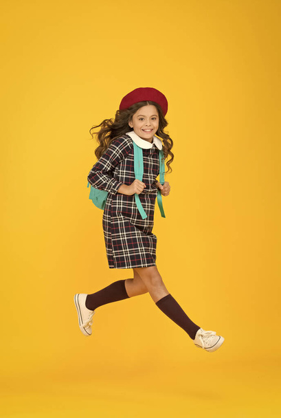 stylish teen college student jumping. little girl with backpack going to school. education concept. school and fashion. child in pupil uniform. kid in french beret on yellow background. hurry up - Foto, immagini
