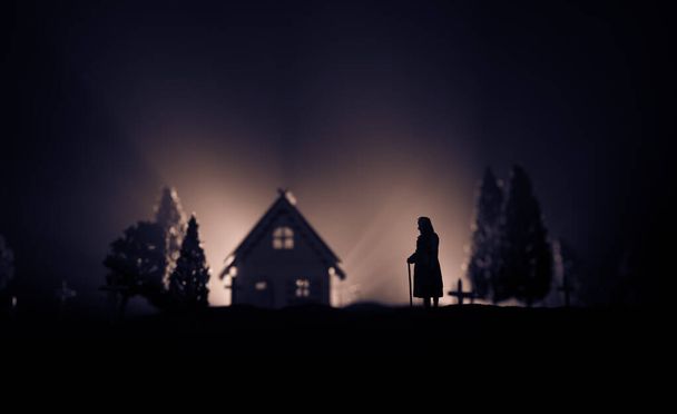 夜に墓地を杖で歩く老婦人のシルエット。ホラーハロウィンのコンセプト。光と霧でアートワークの装飾。選択的焦点 - 写真・画像