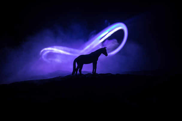 Siluetti hevosen pienoiskoossa seisoo sumuinen yö. Luova pöydän koristelu värikkäällä taustavalolla sumussa. Valikoiva painopiste - Valokuva, kuva