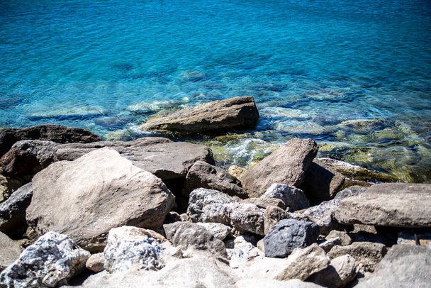 A closeup shot of big stones in a blue seashore - Fotó, kép