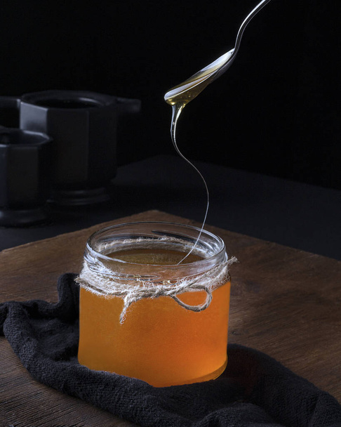 Ein vertikaler Schuss eines Löffels, der Honig aus einem Glas testet - Foto, Bild