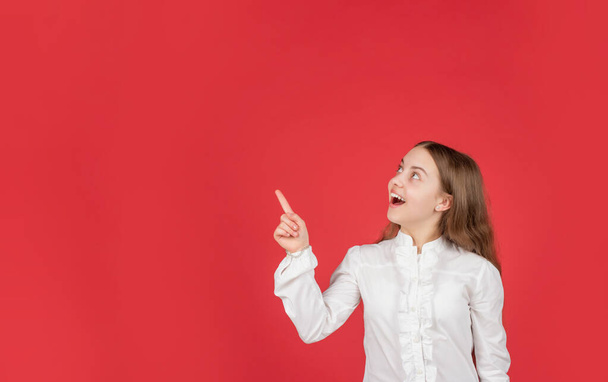 amazed child in white shirt pointing finger on red background copy space, advertisement - Foto, Imagen