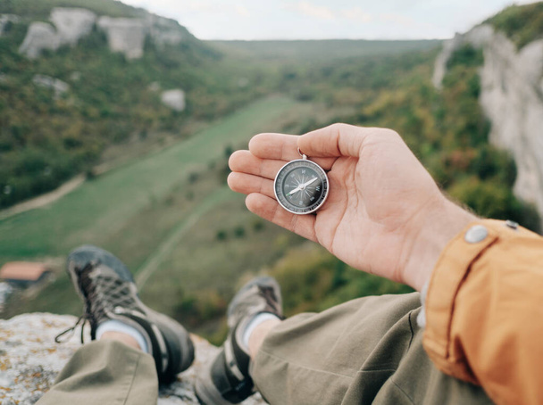 Man sits on the edge of a cliff and holds a compass in the background view of the canyon. - Foto, Imagen