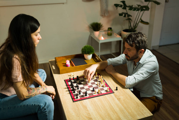 Χαλαρός νεαρό ζευγάρι παίζει σκάκι στο σαλόνι κατά τη διάρκεια της βραδιάς μετά την επιστροφή στο σπίτι από την εργασία  - Φωτογραφία, εικόνα