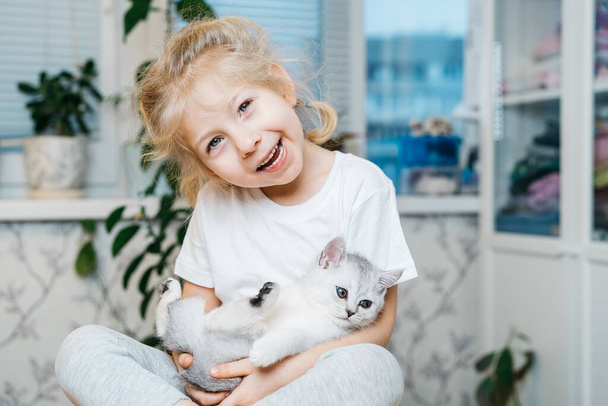 child playing with little cat. A little girl holds a white kitten. A little girl snuggles up to a cute pet while sitting in the living room of the house.Children and pets.  - Фото, изображение