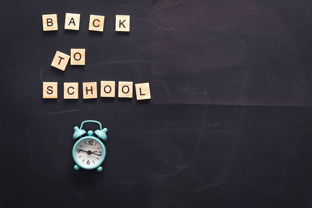 Lettering back to school on abstract textural chalk rub on graphite board or chalkboard background with alarm clock. School education, dark wall background or learning concept. Copy space - Fotoğraf, Görsel