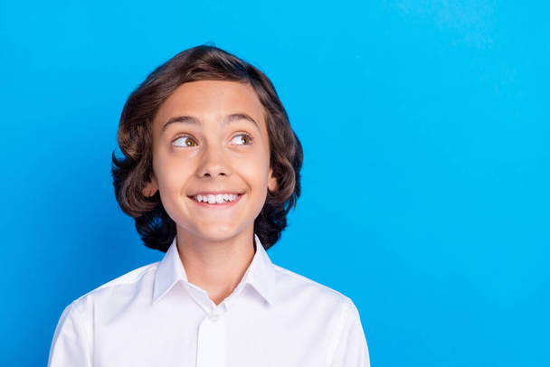 Fotografie zasněný roztomilý školní chlapec nosit formální oblečení s úsměvem vypadající prázdný prostor izolované modré barvy pozadí - Fotografie, Obrázek