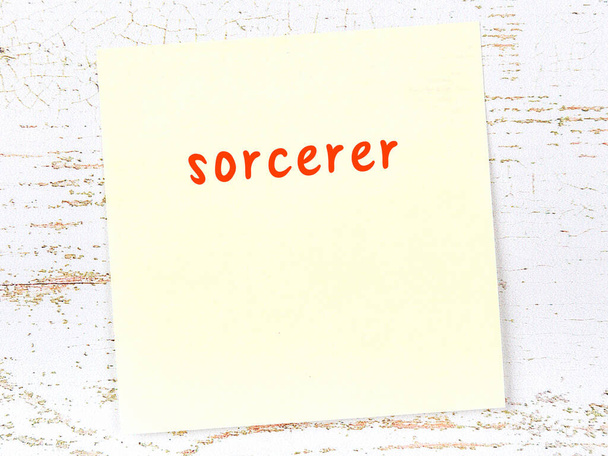Concept of reminder about sorcerer. Yellow sticky sheet of paper on wooden wall with inscription - Photo, image