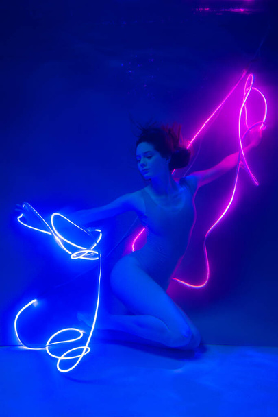 Gimnastyczka rytmiczna tańcząca pod wodą z neonowymi wstążkami. Wolne nurkowanie. Miękkie skupienie. - Zdjęcie, obraz