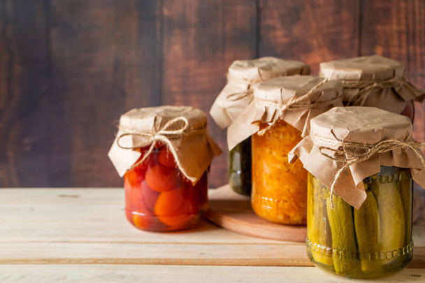 Jars of fermented vegetables on a wooden background. Home made canned cucumbers, tomatoes and sauerkraut. - Photo, Image