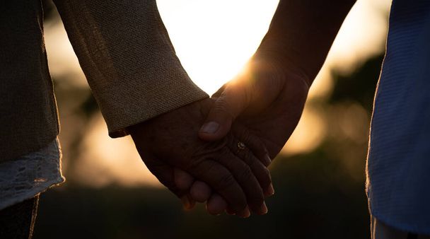 Concept d'amitié, d'amour et de Saint Valentin. Un couple de personnes âgées heureux tenant la main pendant le coucher du soleil, symbole d'amour, mariage heureux, soins de santé seniors et relation. - Photo, image