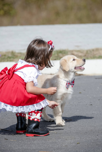 Hermoso niño en vestido rojo y gafas de sol jugando con Golden Retriever perro . - Foto, imagen