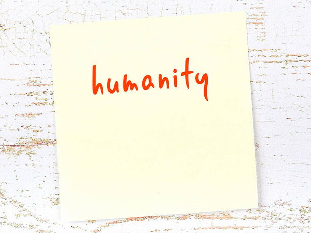 Concept de rappel sur l'humanité. Feuille de papier collante jaune sur mur en bois avec inscription - Photo, image