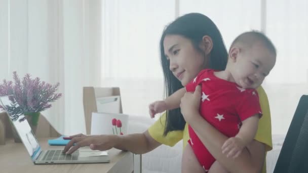 赤ちゃんを抱える母親と幸せな家族、自宅でインターネットにラップトップコンピュータで働いている、専門家とノートブックを使用して娘を保持するお母さん、ビジネスと家庭の概念から仕事. - 映像、動画