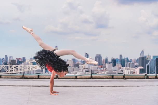 asian girl ballerina dancer performing ballet dance on rooftop of highrise building in city - Фото, изображение