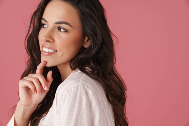 Happy beautiful brunette woman smiling and looking aside isolated over pink background - Foto, afbeelding