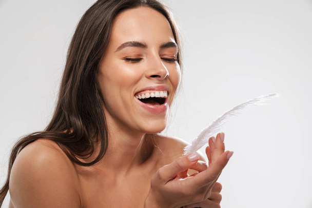 Beautiful shirtless joyful girl laughing while posing with feather isolated over white background - Φωτογραφία, εικόνα