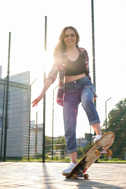 Woman riding a skateboard on street. Skater girl on a longboard. Cool female skateboarder at sunset. Carefree female skater 20s enjoying freedom youth lifestyle Hobby - Фото, изображение