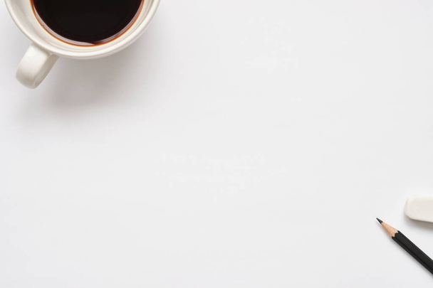 Taza de café blanco, lápiz negro y borrador blanco sobre fondo blanco, vista superior, composición plana, espacio de copia para texto. - Foto, imagen