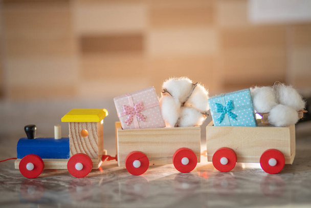 Children's wooden steam locomotive with carriages, transport carries a cotton flower and gifts for the holiday, children's play, wooden constructor, holiday concept. - Photo, Image