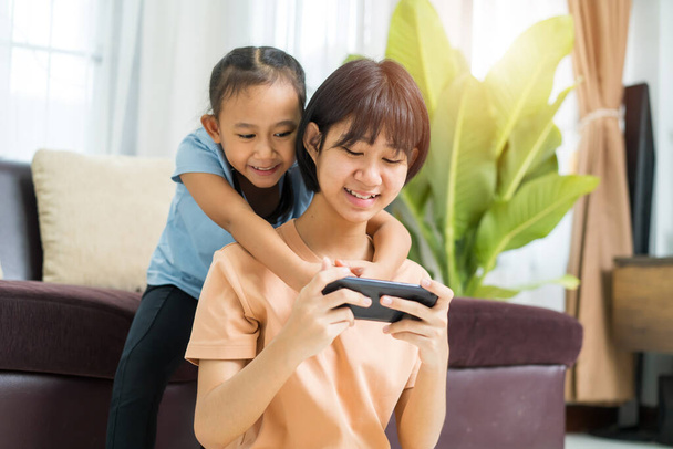 Happy Asian girl with sister play on the smart phone together at home - Foto, imagen