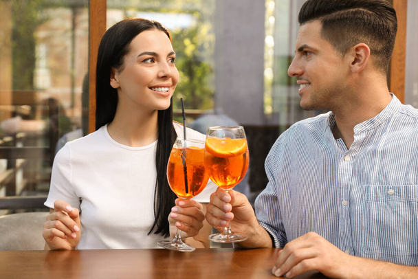 Happy couple clinking glasses of Aperol spritz cocktails outdoors - 写真・画像