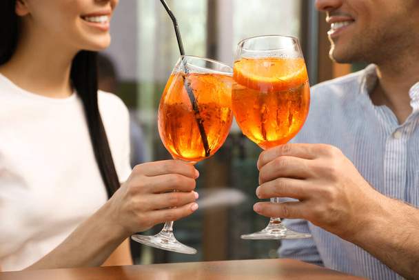 Couple clinking glasses of Aperol spritz cocktails outdoors, closeup - Фото, изображение