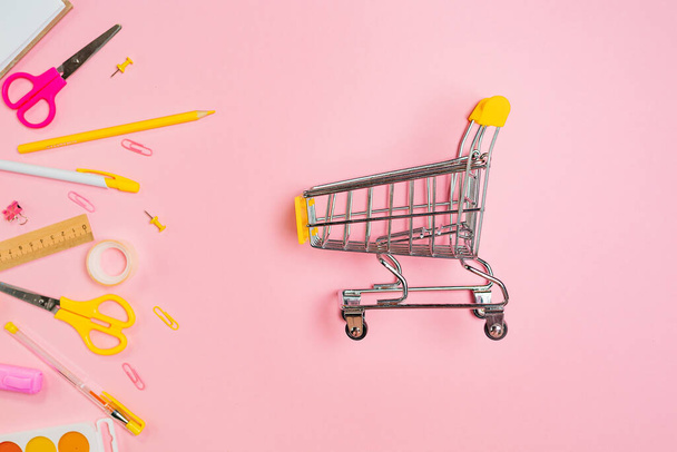 Composition of copybook, shopping and yellow office supplies on pink background. Flat lay. Concept of back to school and consumerism. - Foto, imagen