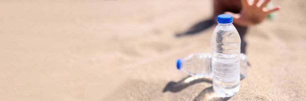 Ο άνθρωπος φτάνει για ένα μπουκάλι νερό που στέκεται στην άμμο - Φωτογραφία, εικόνα