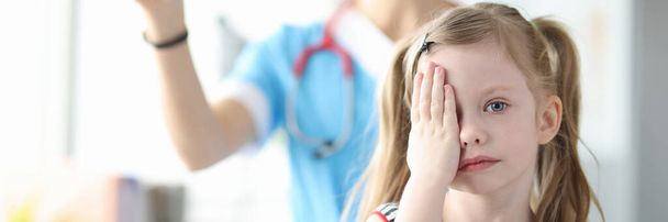 Маленька дівчинка прикриває очі рукою в офтальмолога
 - Фото, зображення