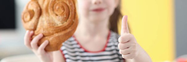 Little girl eating big bun and showing thumb up closeup - Foto, Imagem
