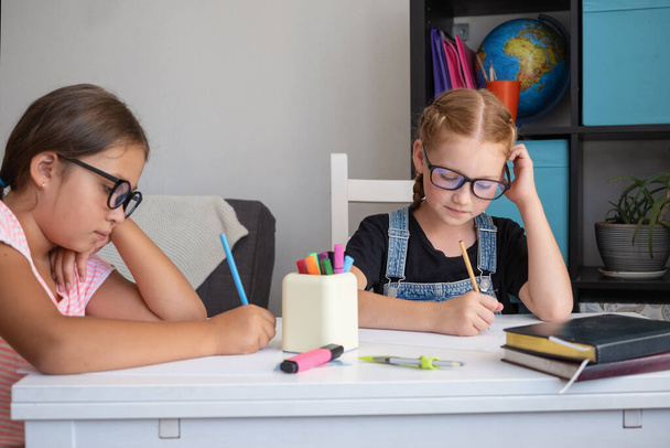 Dwie białe dziewczyny w okularach uczą się w domu, odrabiają lekcje. - Zdjęcie, obraz