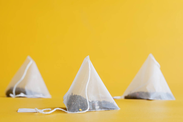 Weiße Pyramiden-Teebeutel mit schwarzem Tee, aromatisiert mit Früchten und Beeren auf leuchtend gelbem Hintergrund. Nachahmung der altägyptischen Pyramiden. Ein Getränk für Langleber. Geringe Schärfentiefe. Makro - Foto, Bild