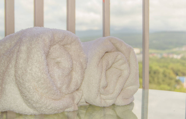 Primer plano de dos rollos de toallas de rizo blanco que yacen sobre una mesa de vidrio transparente en el balcón, el efecto de la reflexión. - Foto, Imagen