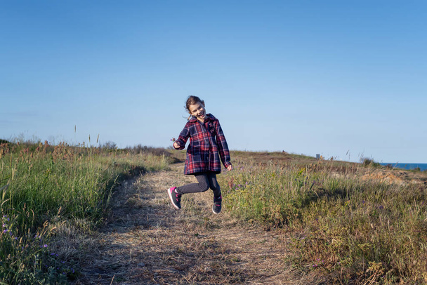Happy little girl jumping and enjoying life on a spring path along picturesque coastline - Valokuva, kuva