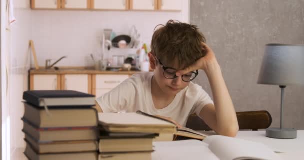 Chłopiec w okularach siedzi w domu wśród książek i czyta. Uczeń odrabia lekcje. Dociekliwy chłopiec. - Materiał filmowy, wideo