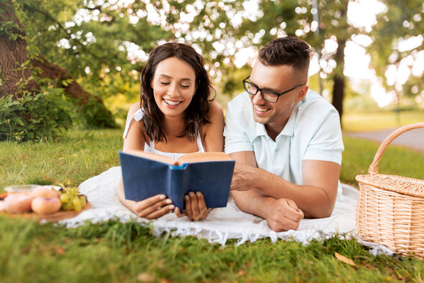 happy couple reading book on picnic at summer park - Fotó, kép