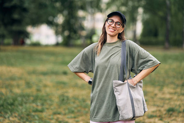 Mujer joven con gafas con bolsa ecológica de algodón vacía, diseño de maqueta. - Foto, Imagen