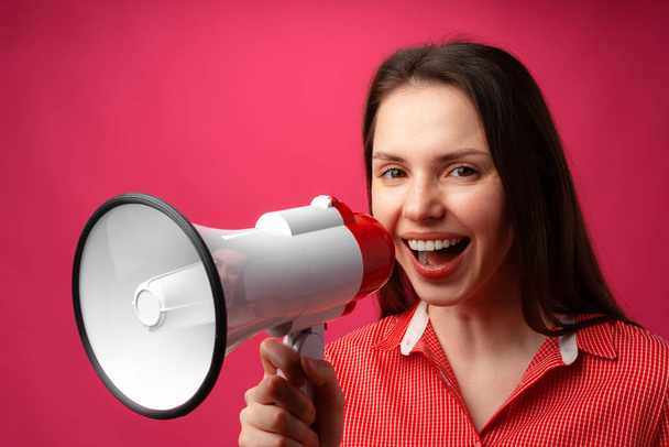 Young brunette woman shouting in megaphone against pink background - Foto, Imagen