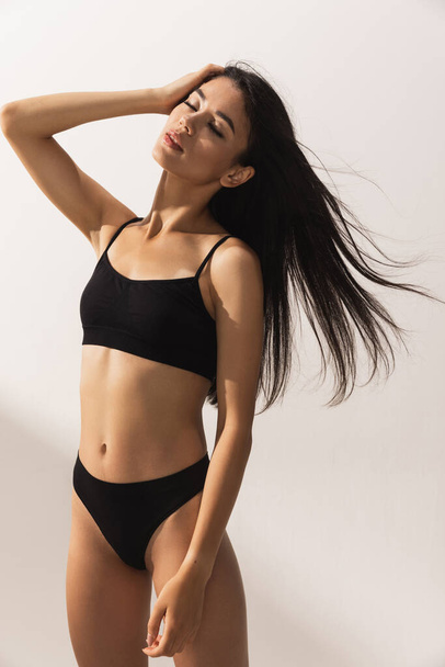 Studio image of young beautiful woman with slim figure in black underwear posing over white studio background - Photo, image