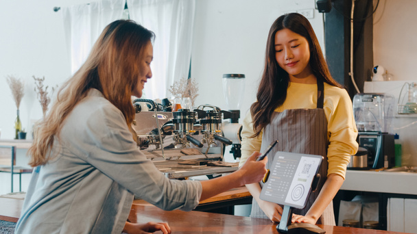 Fiatal Ázsia női önkiszolgáló használja a mobiltelefon fizetés érintésmentes tabletta a kávézó étteremben. A lány barista beszél, megrendeléseket kap a kávézó bárpultjánál. Tulajdonos kisvállalkozás. - Fotó, kép