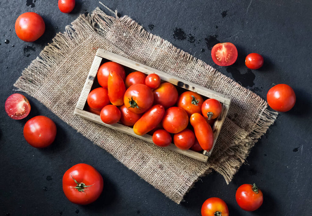 Tomates rojos frescos en caja de madera sobre fondo negro. Piso tendido, vista superior - Foto, imagen