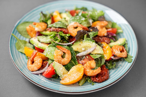 Un piatto d'insalata con gamberetti, rucola e altre verdure, un piatto su un tavolo grigio, cibo per la salute. - Foto, immagini